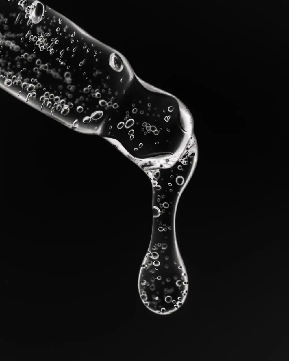 Goutte de sérum translucide suspendue à une pipette en verre, sur fond noir